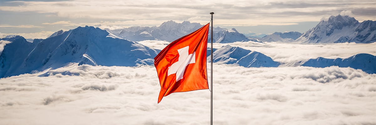 Swiss flag with mountains in the background above the clouds